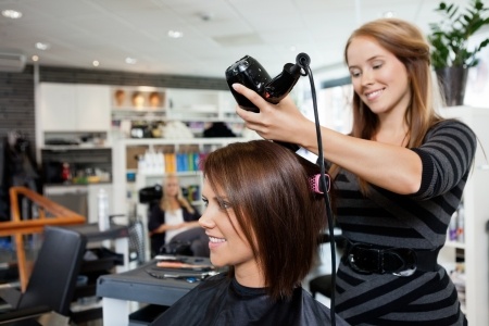 Coiffeuse en train de sécher les cheveux d'une cliente